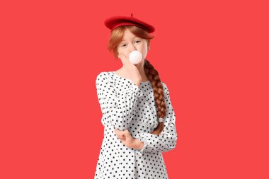 Kızıl arka planda sakız üfleyen kızıl saçlı tatlı bir genç kız.