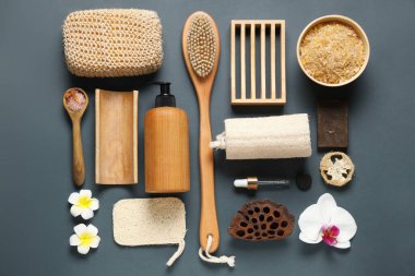 Farklı banyo malzemeleri, çiçekler ve gri arka planda bir kase deniz tuzu içeren kompozisyon.