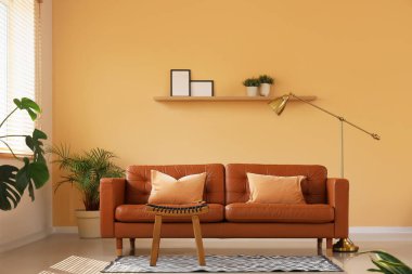 Deri kahverengi kanepe, masa ve zemin lambası şık oturma odasının içindeki bej duvarın yanında.