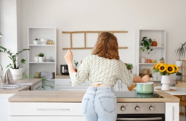 Havalı genç bir kadın mutfakta dans edip yemek yapıyor.
