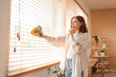 Toza alerjisi olan genç bir kadın pencereyi temizlerken kör ediyor.