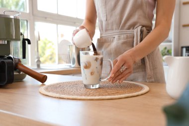 Genç bayan mutfaktaki masada buzlu latte yapıyor, yakın plan.