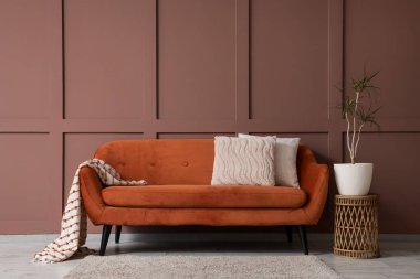 Oturma odasının iç tarafındaki kahverengi duvarın yanında rahat bir kanepe, masa ve çiçek.