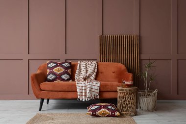 Oturma odasının iç tarafındaki kahverengi duvarın yanında rahat bir kanepe, masa ve katlanabilir ekran.