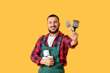 Sarı arka planda boya kutusu ve fırçası olan bir erkek dekoratör.