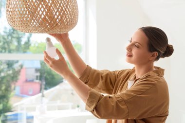 Genç bir kadın ampulü evdeki hasır lambaya takıyor.