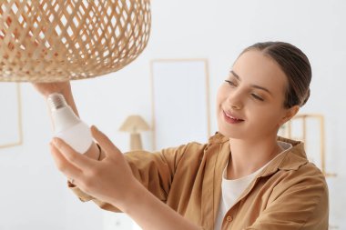 Genç bir kadın ampulü evdeki hasır lambaya takıyor, yakın plan.