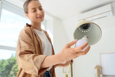 Genç bir kadın evdeki standart lambaya ampul takıyor, yakın plan.