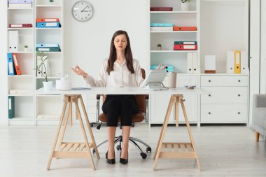 Genç iş kadını ofiste meditasyon yapıyor.