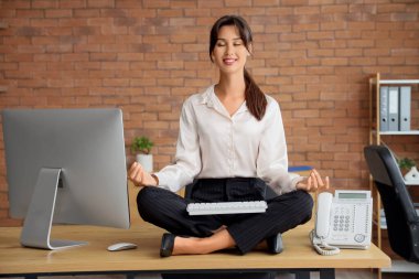 Bilgisayarlı genç iş kadını masada meditasyon yapıyor.