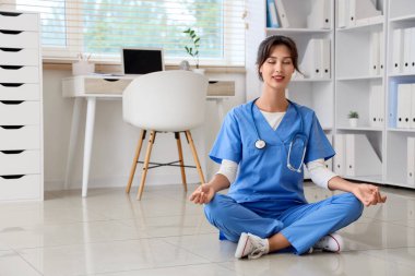 Kadın doktor klinikte yerde meditasyon yapıyor.
