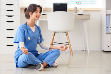 Kadın doktor klinikte yerde meditasyon yapıyor.