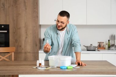 Genç adam mutfakta ilk yardım çantasından damlalar alıyor.