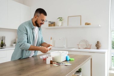 Genç adam mutfaktaki ilk yardım çantasından hap alıyor.