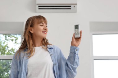 Evinde klima uzaktan kumandalı genç bir kadın var.