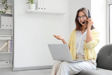 Ofisteki kanepede dizüstü bilgisayarla çalışan kadın teknik destek ajanı.