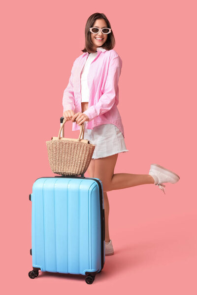 Happy young woman with packed suitcase and bag for travel on pink background