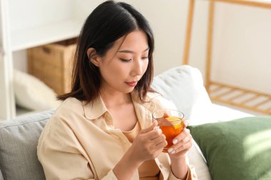 Oturma odasında bir fincan çayla güzel bir Asyalı kadın.