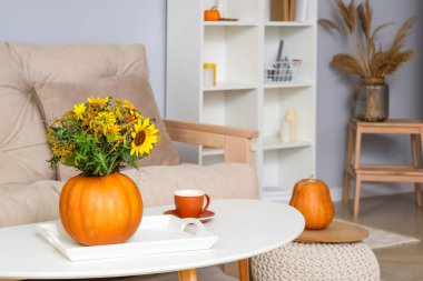 Sonbahar çiçekli balkabağı ve oturma odasındaki masada bir fincan kahve.