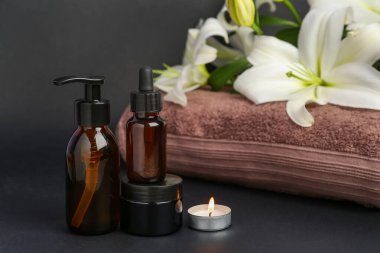 Kozmetik ürünler, temiz havlu ve koyu arkaplanda güzel zambak çiçekleri, yakın plan.