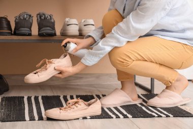 Evde ayakkabılara su püskürtücü sprey sıkan bir kadın.