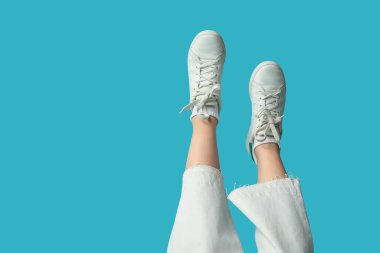 Mavi arka planda beyaz spor ayakkabılı genç bir kadının bacakları.