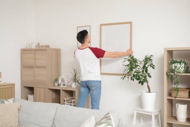Evdeki ışık duvarına boş bir çerçeve asan genç adam.