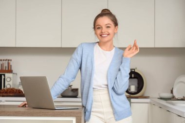 Genç kadın mutfaktaki masada modern dizüstü bilgisayar kullanıyor.