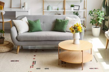 Oturma odasının iç tarafındaki sehpada yabani çiçekler olan rahat bir kanepe ve vazo.