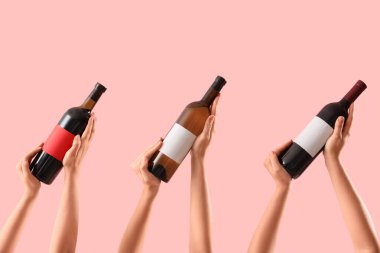 Pembe arka planda şarap şişelerini tutan kadın eller.