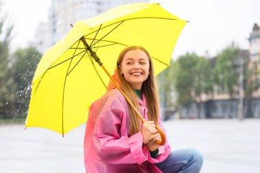 Yağmurlu bir günde açık havada şemsiyeli güzel, mutlu bir kadın oturuyor.