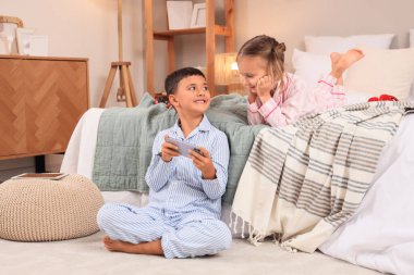 Evde pijamalı, cep telefonlu, video oyunu oynayan sevimli çocuklar.