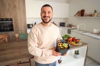 Mutfaktaki gübre kutusunda sebze kırıntıları olan genç bir adam.