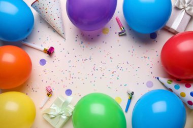 Hediyeli balonlardan yapılmış çerçeve, parti ıslıkları ve bej arka planda konfeti.