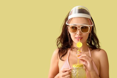 Mayolu, güneş gözlüklü, elinde açık sarı arka planda saman olan limon suyu kavanozu tutan güzel bir kadın.