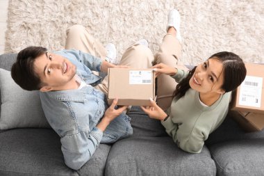 Paket kutulu genç çift evdeki kanepede oturuyor, üst tarafta.