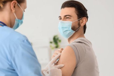 Tıbbi maskeli genç adam klinikteki doktordan aşı alıyor.