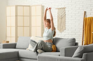 Evdeki gri kanepede uzanan güzel genç bir kadın.