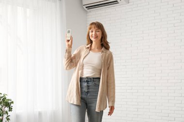 Evinde klima uzaktan kumandalı genç bir kadın var.