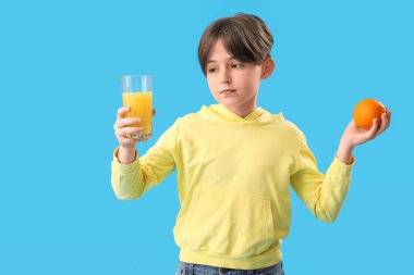 Mavi arka planda portakal suyu ve bir bardak meyve suyu olan küçük çocuk.