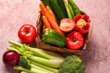Pembe arka planda farklı taze sebzelerle dolu bir sepet.