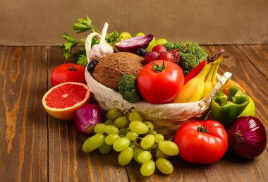 Tahta arka planda farklı taze meyve ve sebzelerle dolu sepet.