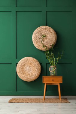 Bambu saplı vazo, renkli duvarın yanındaki ahşap masada.