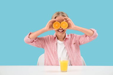 Mavi arka plandaki masada portakallı ve bir bardak meyve suyu olan küçük çocuk.