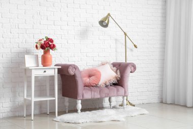 Beyaz tuğla duvarın yanındaki sehpanın üzerinde şakayık çiçekleri olan rahat bir koltuk ve vazo.