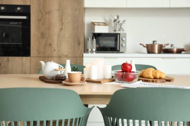 Modern mutfakta kahve, elma ve yanan mumlarla dolu ahşap masa.