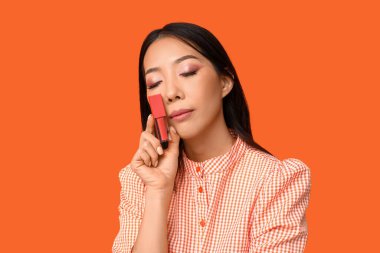 Turuncu arka planda sıvı ruj olan güzel bir Asyalı kadın.