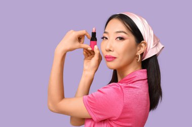 Güzel bir Asyalı kadın, rujlu, eli leylak arkaplanda kalp yapıyor.