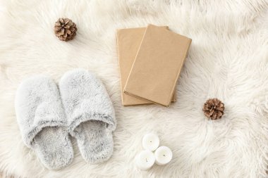 Yumuşak terlikler, mum ve kürk halısı üzerine kitaplar.