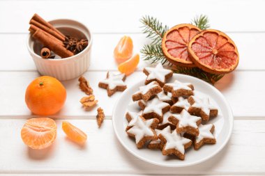 Lezzetli yıldızlı kompozisyon Noel kurabiyeleri, portakallı kurutulmuş parçalar, mandallar, baharatlar ve köknar ağacı dalları hafif ahşap arka planda.